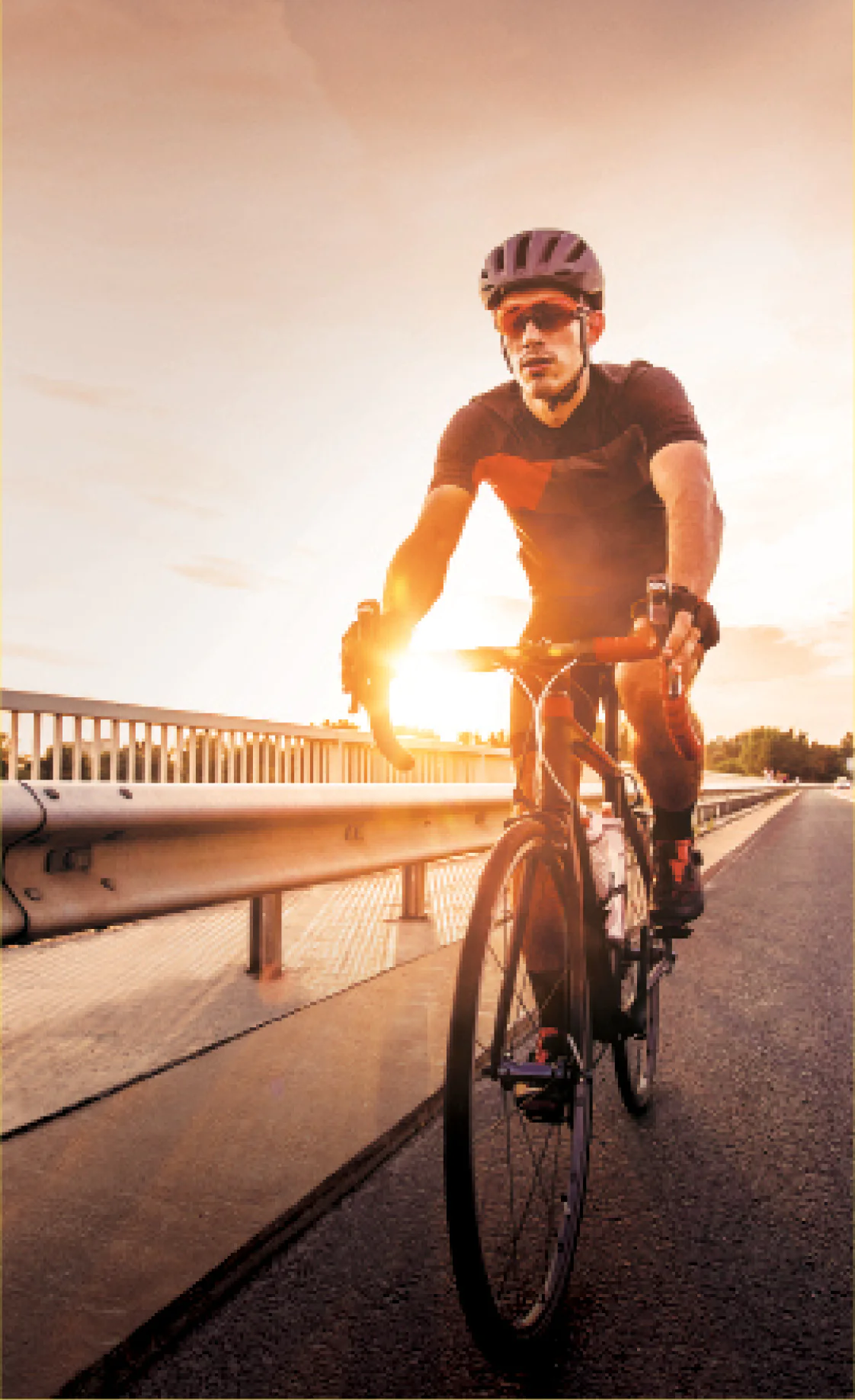 Homem pedalando uma bicicleta sobre uma ponte ao pôr do sol, com cores quentes refletindo no céu.